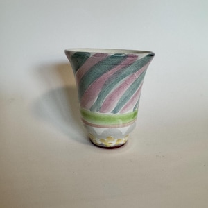 Op de afbeelding: Een keramische vaas met een uitlopende bovenkant, met diagonale groene en roze strepen. De vaas heeft een groene en gele band bij de basis, met een decoratief patroon en een rode basis.
