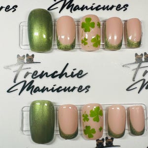 May include: Set of ten green and nude false nails with a shamrock design. The nails have a green tip and a nude base. The shamrock design is on the nude nails. The nails are arranged in two rows of five. The text "Frenchie Manicures" is visible in the image.