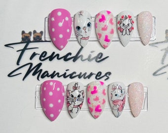 May include: Set of ten pink and white press-on nails with a pink polka dot design, a white glitter design, and a white design of a cartoon cat with pink accents. The nails are arranged on a white display card with the text "Frenchie Manicures" printed in black.