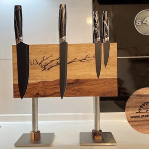 Op de afbeelding: Een houten messenhouder met een magneetstrip om messen te houden. De houder heeft een standaard en is gemaakt van hout met een natuurlijke houtnerf. De houder heeft een gebrand ontwerp van een tak. De houder heeft de tekst "S4Y" en "handmade" erop. De houder heeft de website "www.station4you.de" erop.