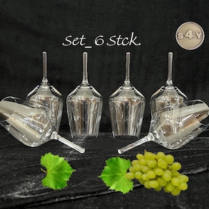 Könnte beinhalten: Set aus sechs transparenten Weingläsern mit langen Stielen, angeordnet auf einer dunklen Oberfläche. Die Gläser werden von grünen Weinblättern und einer Traube begleitet. Der Text "set_6 stck." ist sichtbar.