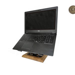 Könnte beinhalten: Ein schwarzer Laptop-Computer auf einem Holzständer. Der Laptop hat eine vollständige Tastatur und einen großen Bildschirm. Der Ständer ist aus Holz und hat ein Metallscharnier. Ein kleines, rundes, bronzefarbenes Emblem befindet sich in der oberen rechten Ecke.