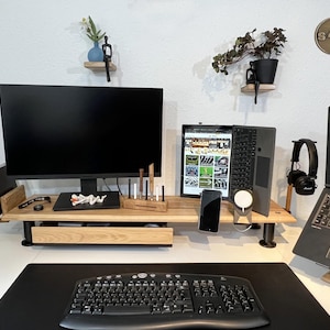 Peut inclure: Un bureau moderne avec un grand écran, un ordinateur portable et une tablette. Le bureau est en bois clair et comprend un clavier, un tapis de souris et divers accessoires. Des plantes décoratives et une petite étagère avec une figurine sont également visibles.