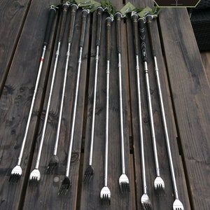 Peut inclure: Un ensemble de 12 outils de réparation de club de golf argentés avec des poignées noires et vertes. Les outils ont une extrémité en forme de fourchette et un long manche fin. Les outils sont disposés en rangée sur une surface en bois.