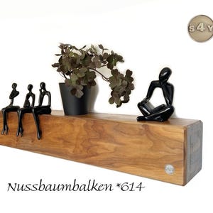 Könnte beinhalten: Ein Holzregal mit natürlicher Oberfläche, auf dem drei schwarze abstrakte Figuren am Rand sitzen. Auf dem Regal befinden sich auch eine Topfpflanze mit dunkelgrünen Blättern und eine schwarze Skulptur einer lesenden Person. Der Text "Nussbaum balken *614" steht darunter.