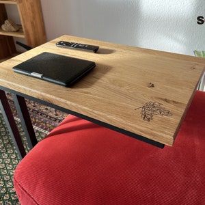 Op de afbeelding: Een houten tafel met een zwart metalen frame, een zwarte e-reader en een afstandsbediening erop. De tafel staat op een rode bank.