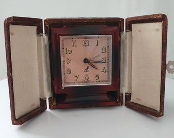 Könnte beinhalten: Ein vintage roter und schwarzer Wecker mit weißem Zifferblatt und goldenen Akzenten. Die Uhr befindet sich in einem braunen Lederetui mit weißer Auskleidung. Das Zifferblatt der Uhr trägt die Aufschrift "Jazz" und "Made in France".