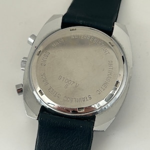 May include: A silver-toned wristwatch with a black leather band. The back of the watch has the text "STAINLESS STEEL BACK", "V 91007", "8", "MADE SWISS", "WATER RESISTANT", and "ANTIMAGNETIC".