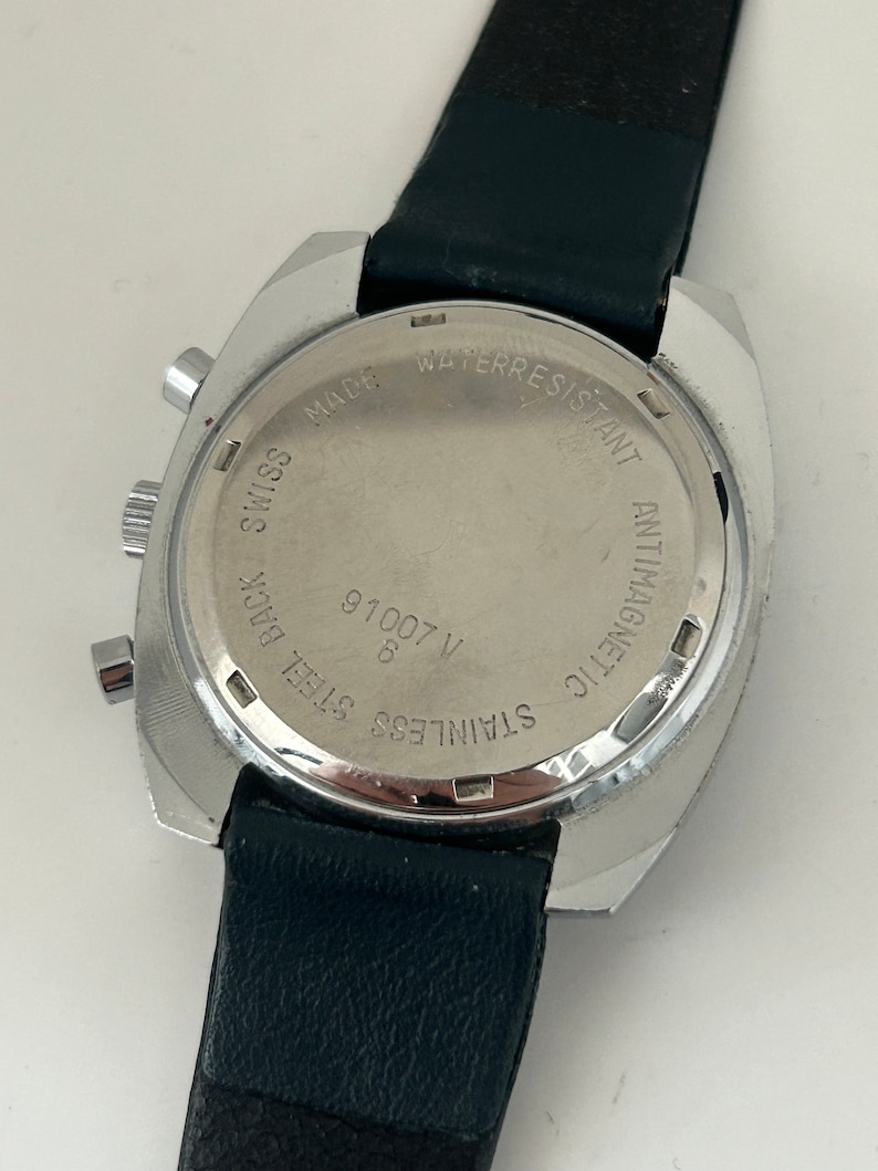 May include: A silver-toned wristwatch with a black leather band. The back of the watch has the text "STAINLESS STEEL BACK", "V 91007", "8", "MADE SWISS", "WATER RESISTANT", and "ANTIMAGNETIC".