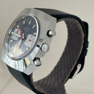 May include: A silver chronograph wristwatch with a black leather band. The watch face has a blue background with white markings and a red second hand. The watch has the word "RENIS" printed on the face.