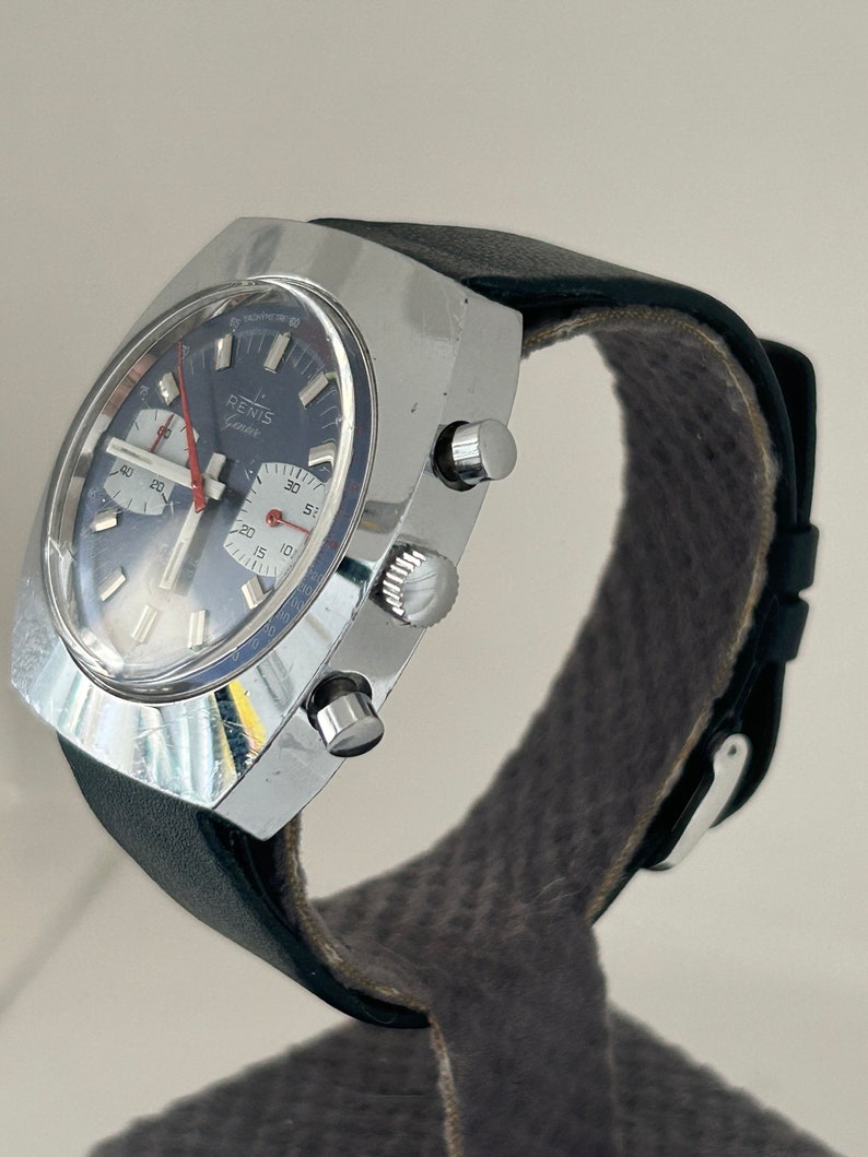 May include: A silver chronograph wristwatch with a black leather band. The watch face has a blue background with white markings and a red second hand. The watch has the word "RENIS" printed on the face.