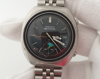May include: A silver Seiko Sports Speed-Timer chronograph wristwatch with a black face and a silver metal band.