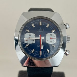 May include: A silver chronograph wristwatch with a blue face and red accents. The watch face features the text "RENIS Gen&egrave;ve" and "TACHYMETRE 60".
