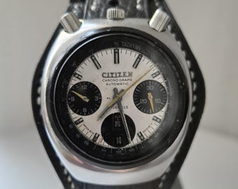 May include: A silver Citizen chronograph wristwatch with a black leather band. The watch face is white with black markings and has a tachymeter scale. The watch has a date window at the 4 o'clock position and the text "Citizen Chronograph Automatic" is printed on the face.