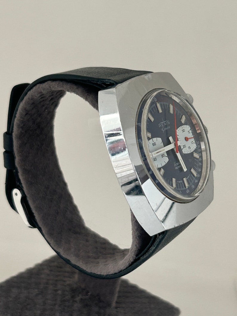 May include: A silver square-shaped chronograph wristwatch with a black face and red second hand. The watch has a black leather band with a white stitching detail.