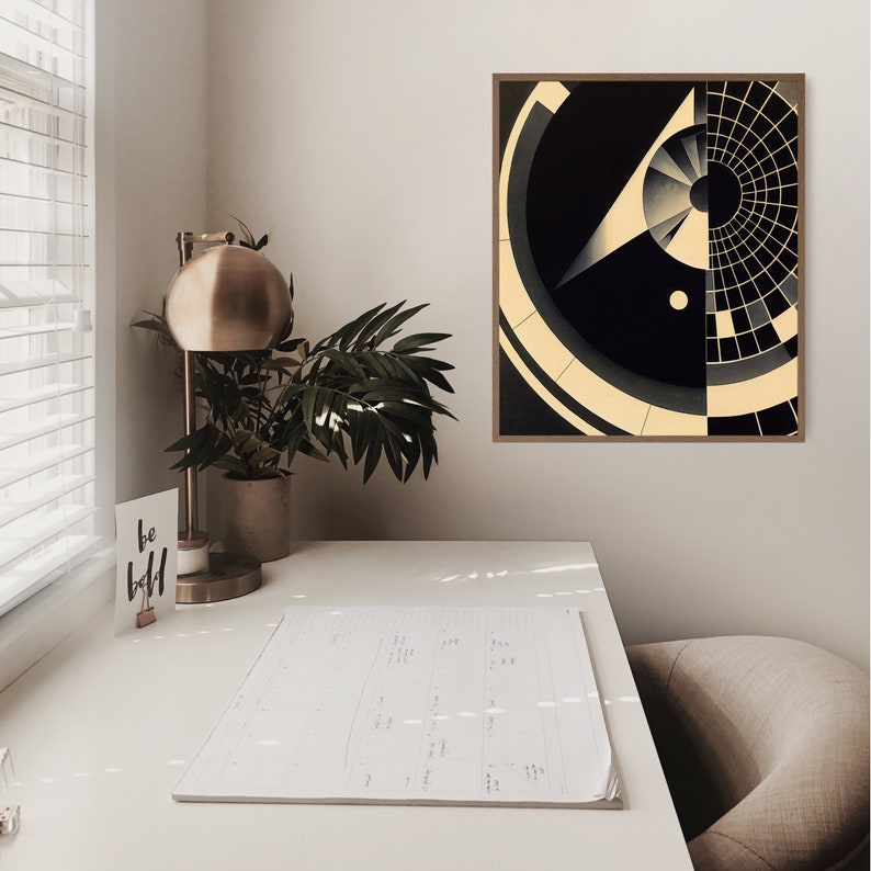 Puede incluir: Una impresi&oacute;n de arte abstracto geom&eacute;trico en blanco y negro con un marco de madera. La impresi&oacute;n est&aacute; colgada en una pared blanca sobre un escritorio blanco con una l&aacute;mpara, una planta y un cuaderno.