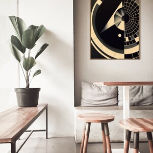 Puede incluir: Una impresi&oacute;n de arte abstracto geom&eacute;trico en blanco y negro con un marco dorado. La impresi&oacute;n presenta un c&iacute;rculo con un c&iacute;rculo m&aacute;s peque&ntilde;o en su interior y una forma triangular con una l&iacute;nea que se extiende desde el punto superior. La impresi&oacute;n est&aacute; colgada en una pared blanca sobre una mesa de madera y dos taburetes de madera.