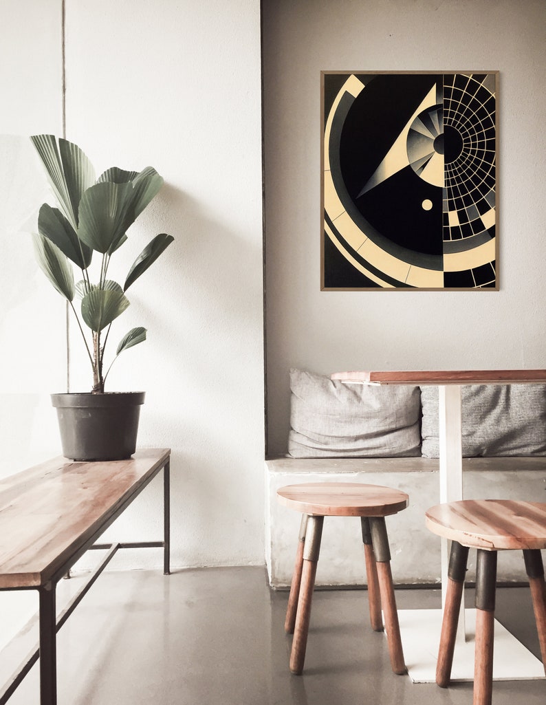 Puede incluir: Una impresi&oacute;n de arte abstracto geom&eacute;trico en blanco y negro con un marco dorado. La impresi&oacute;n presenta un c&iacute;rculo con un c&iacute;rculo m&aacute;s peque&ntilde;o en su interior y una forma triangular con una l&iacute;nea que se extiende desde el punto superior. La impresi&oacute;n est&aacute; colgada en una pared blanca sobre una mesa de madera y dos taburetes de madera.