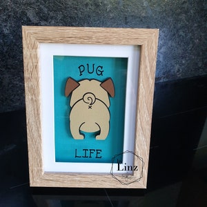 May include: A framed wooden sign with a teal background and a brown cutout of a pug's rear end. The sign says "Pug Life" and is signed "by Linz".