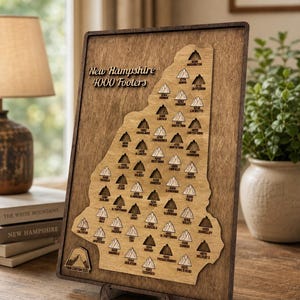 May include: Wooden plaque featuring a map of New Hampshire with the text "New Hampshire 4000 Footers." The map highlights various mountain peaks with their elevations. The plaque is displayed on a wooden stand, showcasing a rustic aesthetic.