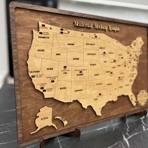 May include: A wooden map of the United States with the locations of National Hockey League teams marked. The map is on a brown wooden base with a stand.