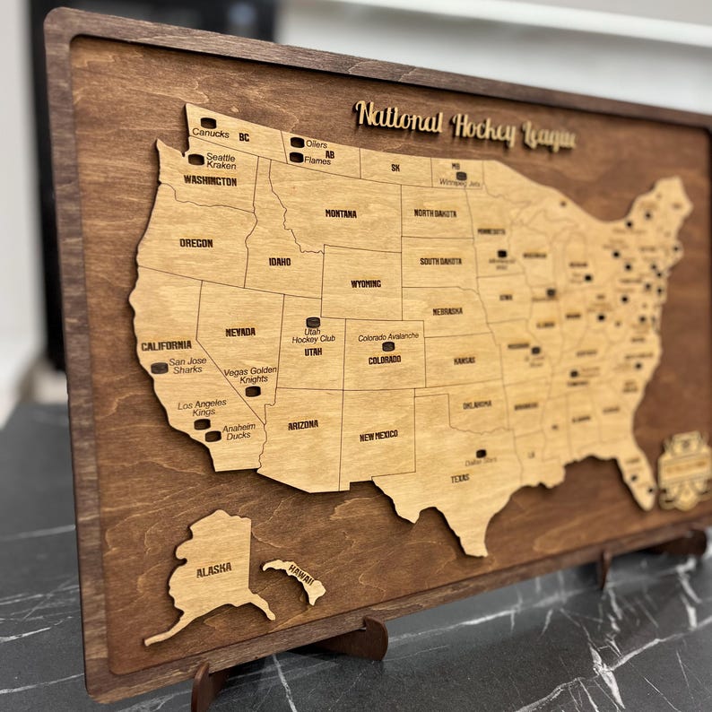 May include: A wooden map of the United States with the locations of National Hockey League teams marked. The map is on a brown wooden base with a stand.
