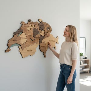 May include: A wooden wall map of Switzerland composed of individual pieces in varying shades of brown and tan. The map features engraved labels for cantons including Vaud, Bern, Valais, Ticino, and Graubünden, mounted on a plain white wall.