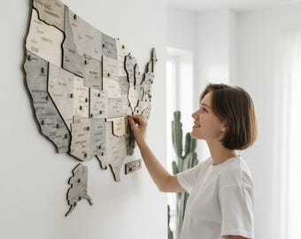 May include: A large wall-mounted map of the United States constructed from individual wooden pieces in varying shades of gray and natural wood tones. The map features engraved state names and borders, with small green pins placed on various locations.