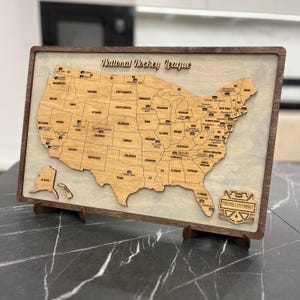 May include: A wooden map of the United States with the locations of National Hockey League teams marked. The map is framed in dark wood and has a small plaque at the bottom that says "The Miller Family".
