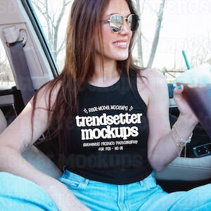 May include: A black tank top with the text "trendsetter mockups" in white. The person is wearing sunglasses and holding a clear plastic cup with a green straw. The person is sitting in a car.