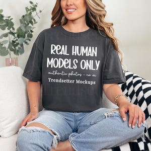 Może przedstawiać: Ciemnoszara koszulka z białym napisem "REAL HUMAN MODELS ONLY". Koszulka ma również napis "authentic photos - no ai Trendsetter Mockups". Modelka ma na sobie jasnoniebieskie dżinsy.