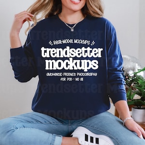 May include: A navy blue long-sleeve sweatshirt with the text "trendsetter mockups" in white. The sweatshirt is part of a product mockup, perfect for showcasing designs. The model is wearing blue jeans and white sneakers.