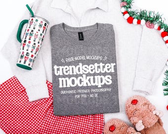 May include: A gray crewneck t-shirt featuring the white text REAL-MODEL MOCKUPS trendsetter mockups AUTHENTIC PRODUCT PHOTOGRAPHY FOR POD NO AI, a nutcracker-patterned tumbler, a white waffle-knit sweater, red gingham pants, and fuzzy slippers.