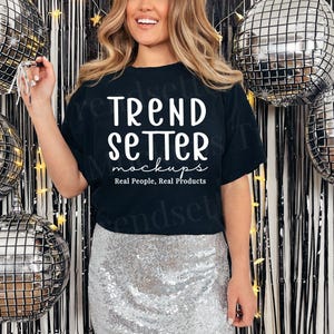 May include: A black t-shirt with the text "Trend Setter mockups Real People, Real Products" in white. The person is wearing a silver sequin skirt. Silver disco balls are in the background.