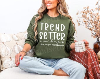 Puede incluir: Una sudadera de cuello redondo color verde oliva con el texto blanco TREND SETTER mockups y el texto más pequeño Real People, Real Products impreso en el frente. La sudadera tiene mangas largas y cuello, puños y dobladillo acanalados.