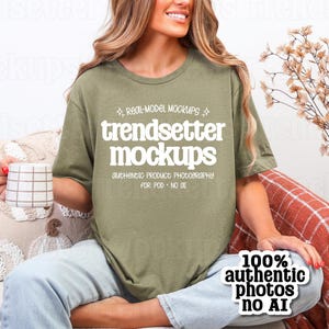 Op de afbeelding: Olijfgroen t-shirt met de witte tekst "trendsetter mockups". De afbeelding bevat ook een wit en bruin geruit mok, een decoratief kussen en een herfstthema-arrangement. Een sticker luidt "100% authentic photos no AI."