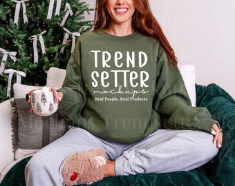 May include: An olive green crewneck sweatshirt featuring the white text "TREND SETTER mockups" and "Real People, Real Products" printed on the front. The sweatshirt has long sleeves and a ribbed collar, cuffs, and hem, worn with light gray sweatpants.