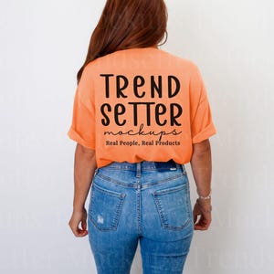 May include: An orange t-shirt with the text "TREND SETTER mockups Real People, Real Products" in black. The model is wearing blue jeans. The shirt is a mock-up for apparel.