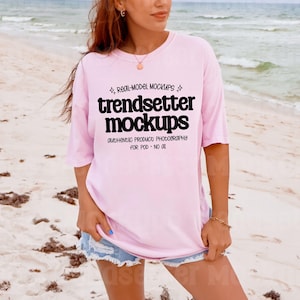 以下が含まれることがあります： 「trendsetter mockups」の黒い文字が入った、明るいピンク色のTシャツ。ビーチで人が着ています。「REAL-MODEL MOCKUPS」と「AUTHENTIC PRODUCT PHOTOGRAPHY FOR POD - NO OI」の文字もプリントされています。