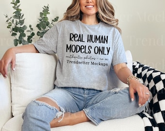Könnte beinhalten: Ein graues, kurzärmeliges T-Shirt mit dem schwarzen Text "REAL HUMAN MODELS ONLY", gefolgt von "authentic photos - no ai" und "Trendsetter Mockups", der auf den Brustbereich des Kleidungsstücks gedruckt ist.