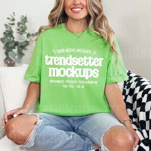 May include: A lime green t-shirt with the text "trendsetter mockups" in white. The shirt is paired with light blue ripped jeans. The model is seated on a white chair with a black and white checkered blanket.