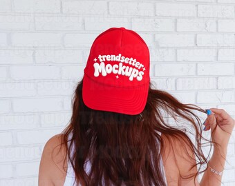 Może przedstawiać: Czerwona czapka bejsbolowa z białym napisem "trendsetter mockups". Czapka jest noszona przez osobę z długimi brązowymi włosami. Tło to biała ceglana ściana.