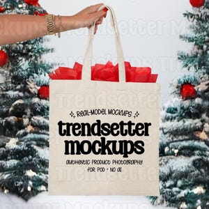 May include: A beige canvas tote bag featuring black text that reads REAL-MODEL MOCKUPS, trendsetter mockups, AUTHENTIC PRODUCT PHOTOGRAPHY, and FOR POD • NO AI. The bag is filled with red tissue paper and has two top handles.