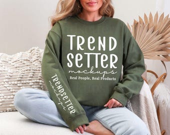 May include: An olive green crewneck sweatshirt featuring the white text TREND SETTER mockups Real People, Real Products on the chest and the vertical text TRENDSETTER mockups printed in white along the right sleeve.