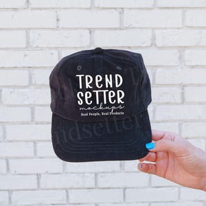 May include: Black corduroy baseball cap with the text "TREND SETTER mockups Real People, Real Products" in white. The cap is held by a hand with blue nail polish.