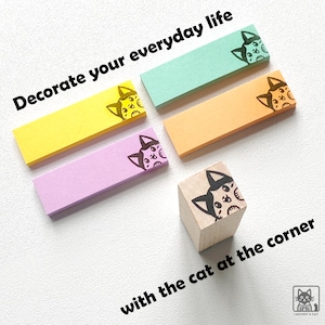 May include: A collection of colorful sticky notes and a wooden stamp featuring a cat design. The sticky notes are in yellow, pink, orange, and teal. Text on the image reads "Decorate your everyday life with the cat at the corner."