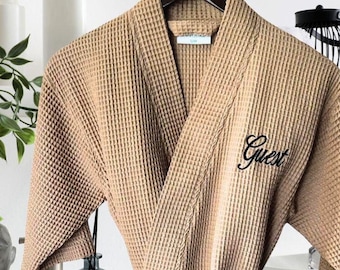 May include: A waffle weave robe in a light brown color with the word "Guest" embroidered on the front.