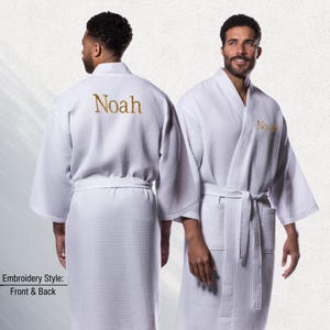 May include: White waffle-weave robe with the name "Noah" embroidered in gold thread on the back and front. The robe has a shawl collar, a waist tie, and pockets. The image shows the front and back of the robe.