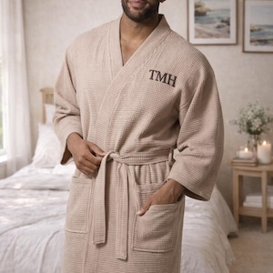 May include: Beige waffle-weave robe with a shawl collar, pockets, and a matching belt. The initials "TMH" are embroidered on the chest. The robe is worn over clothing.