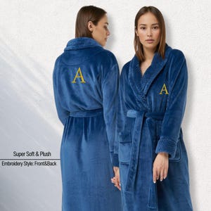 May include: Two plush, blue bathrobes with a gold embroidered "A" on the front and back. The robes have a shawl collar, pockets, and a matching belt. The text "Super Soft & Plush" and "Embroidery Style: Front&Back" is visible.